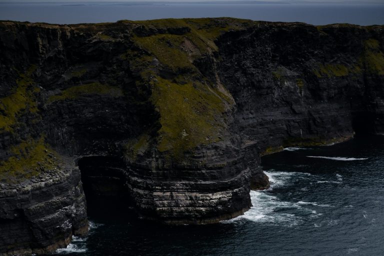 Stunning view of rugged cliffs with ocean waves crashing below on a gloomy day.