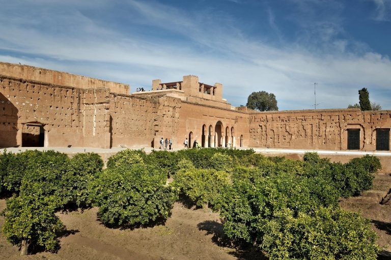 View of historic red walls and lush gardens under a blue sky in Marrakesh, Morocco.