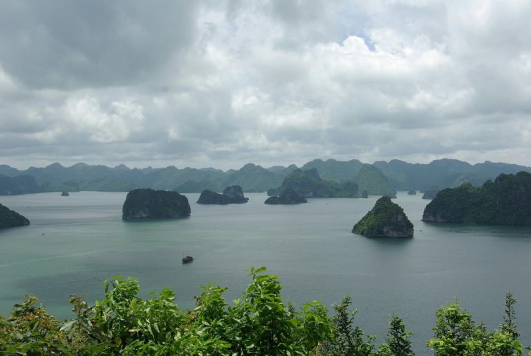 Aerial view of picturesque islands and tranquil waters in Halong Bay under a cloudy sky.