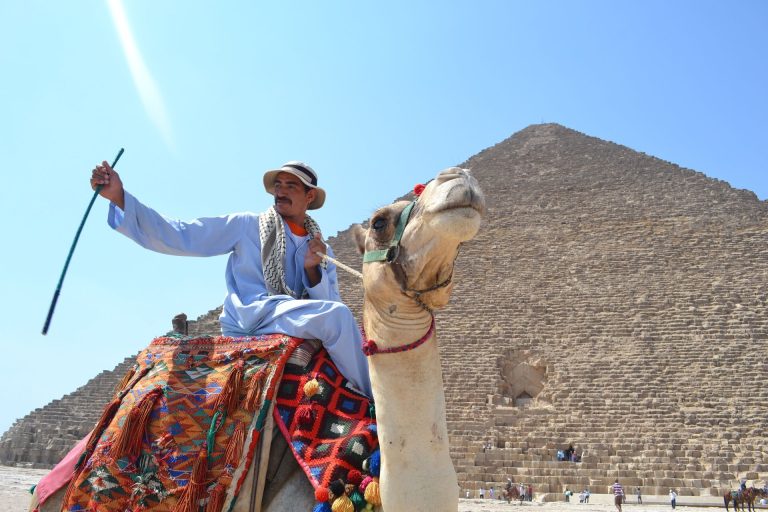 Man riding a camel in front of the Great Pyramid of Giza, a popular tourist attraction in Egypt.