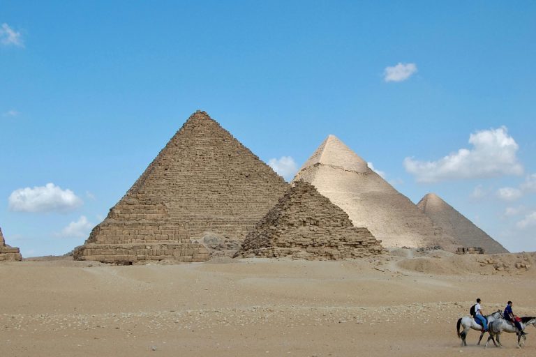 Iconic Giza Pyramids with horses and riders under a clear sky, capturing Egypt's ancient allure.