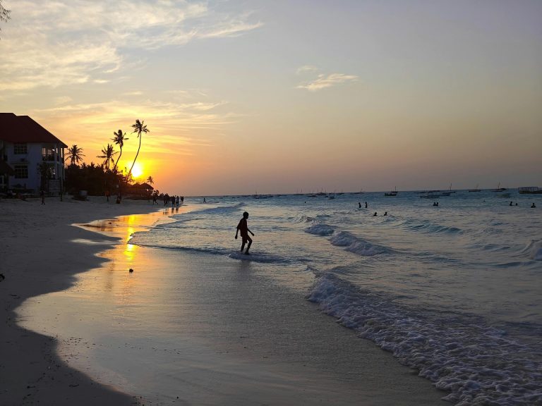 A tranquil beach at sunset featuring silhouettes of people along the shore.