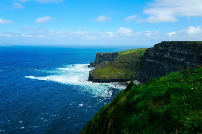 Breathtaking view of the Cliffs of Moher with expansive ocean and lush greenery under a bright sky.
