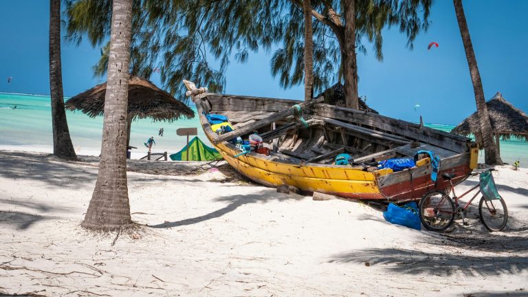 Tropical beach scene in Zanzibar featuring a colorful abandoned boat and bicycle under palm trees.
