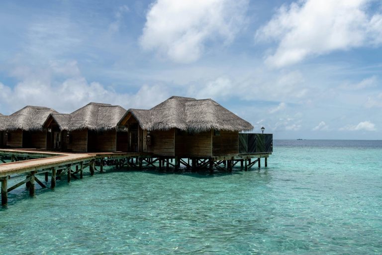 Overwater bungalows with thatched roofs on a turquoise ocean, under a clear blue sky in the Maldives.