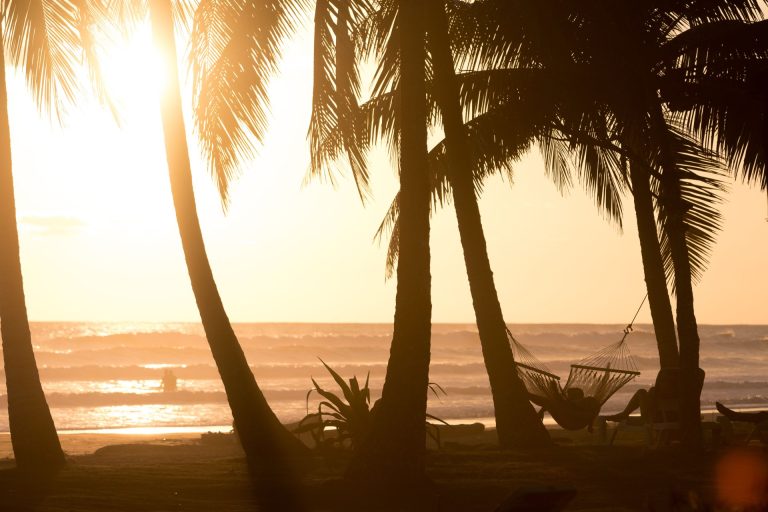 Silhouette of palms and a hammock on a serene Costa Rican beach at sunset.