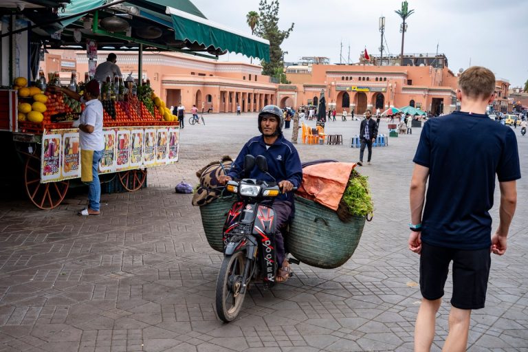 Snapshot of bustling Marrakesh market square with vendor and scooter, capturing local life.