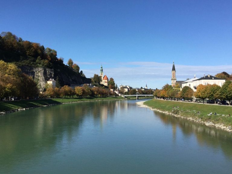 Beautiful autumn view of the riverbank in Salzburg with historic churches and colorful foliage.