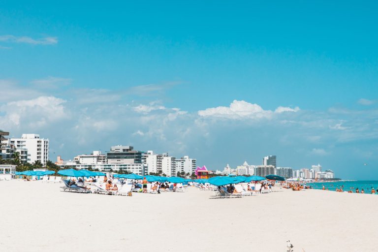 Vibrant Miami Beach scene with blue umbrellas and city skyline under a sunny sky.