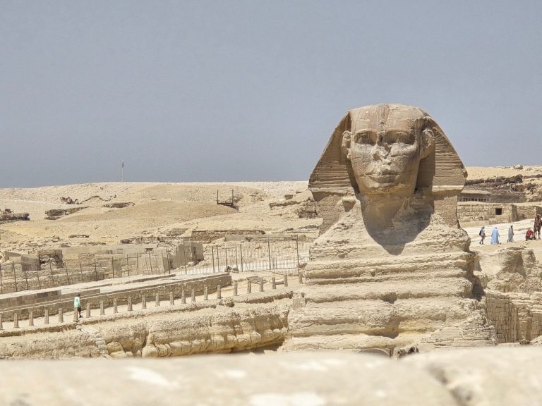 A clear daytime view of the Great Sphinx of Giza, Egypt, surrounded by sandy desert.