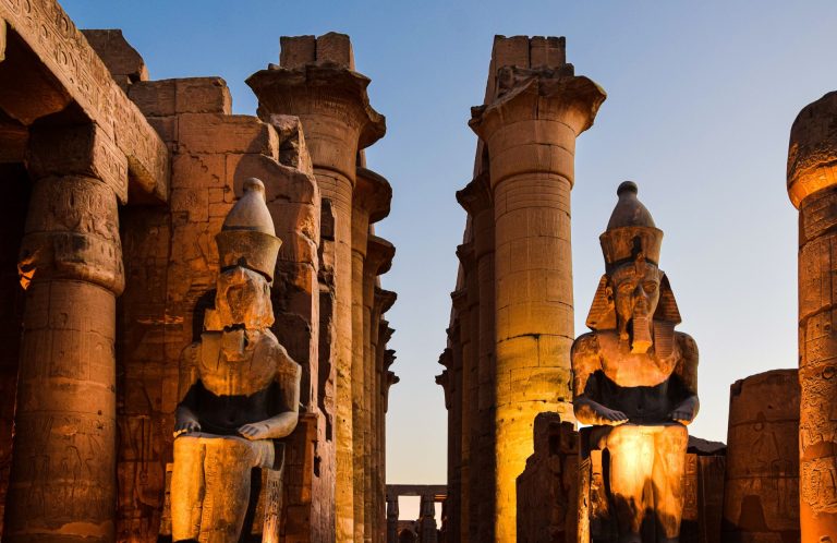 Illuminated statues and columns at Luxor Temple during sunset in Egypt.