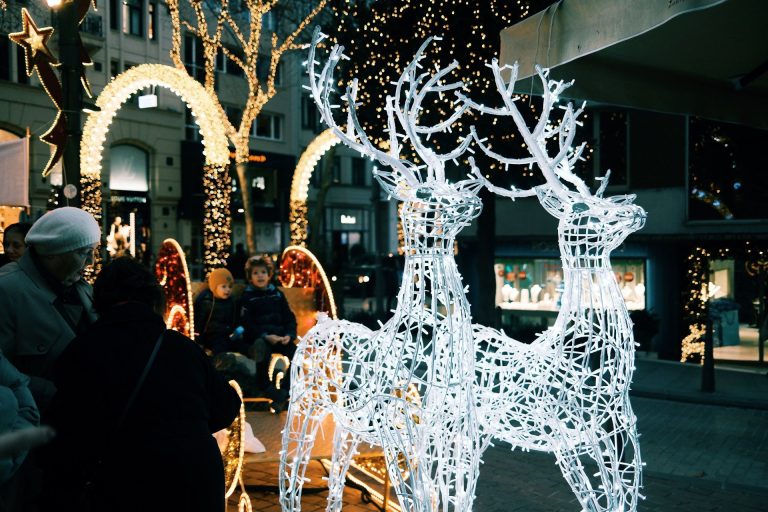 Illuminated reindeer sculptures and people enjoying a festive street display.