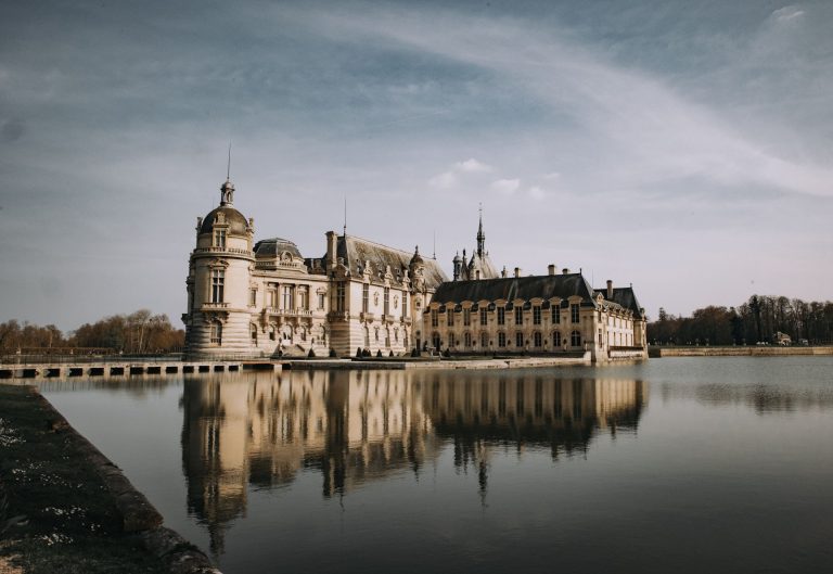 Stunning view of Château de Chantilly with reflection in a serene lake under a clear sky in France.