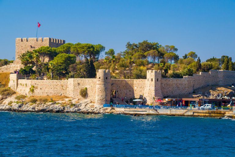 Medieval fortress in Kusadasi, Turkey, with Turkish flag and coastal view.