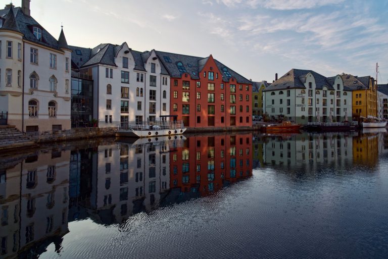 Charming waterfront buildings in Ålesund, Norway with vibrant reflections in the calm sea.