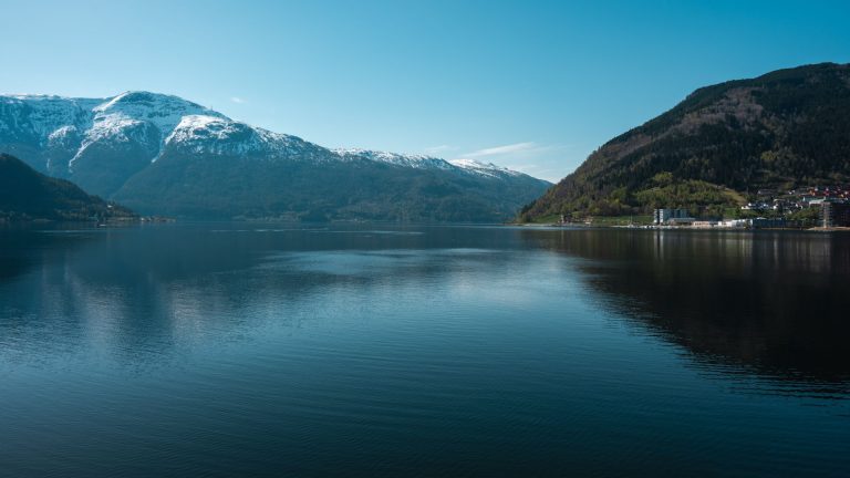 Discover Sogndalsfjøra's tranquil beauty with its snow-capped mountains and calm waters.