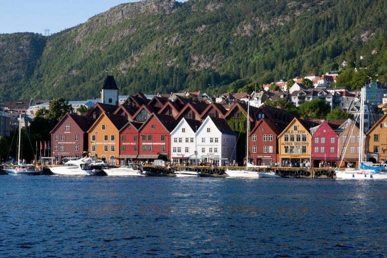 Colorful buildings along Bergen's historic waterfront with boats and lush mountains in view.