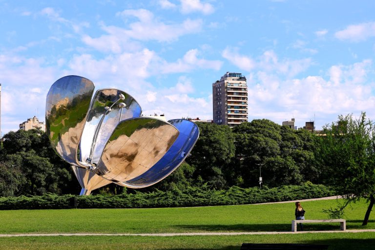 Floralis Generica sculpture in a Buenos Aires park with buildings in the background.