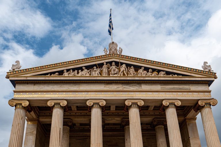 Detailed view of the Academy of Athens facade showcasing classical columns and sculptures under a cloudy sky.