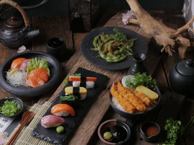 A beautifully arranged variety of sushi, sashimi, and edamame on wooden background.