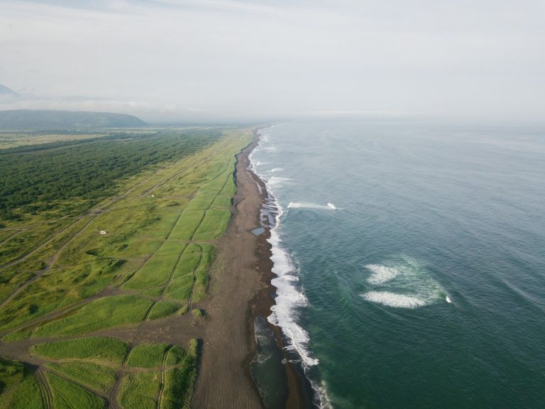 A stunning aerial view of a long coastline with lush green fields and the vast ocean, captured in daylight.