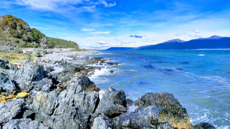 Explore the rocky seacoast of Ushuaia, Argentina, with stunning views of the ocean and distant mountains.