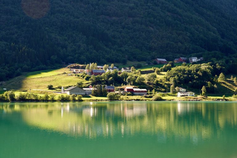 Peaceful rural landscape with green hills and a serene lake reflecting the idyllic village.