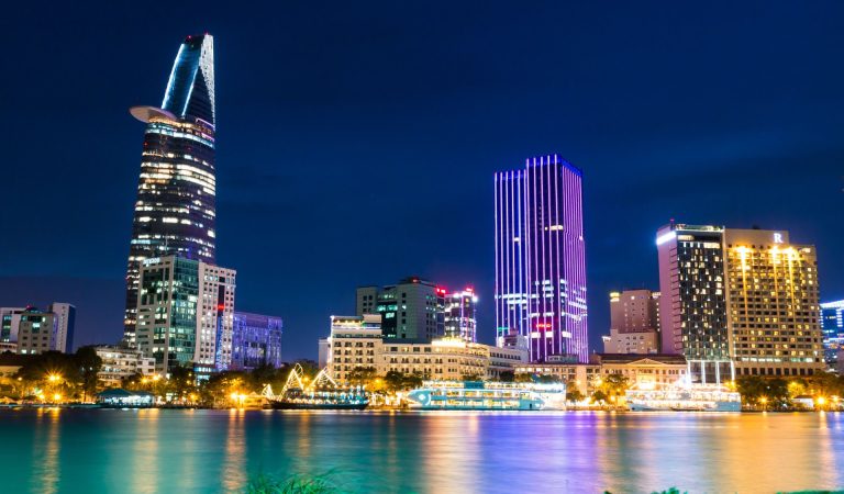 Vibrant night view of Ho Chi Minh City skyline with illuminated skyscrapers reflecting in the river.