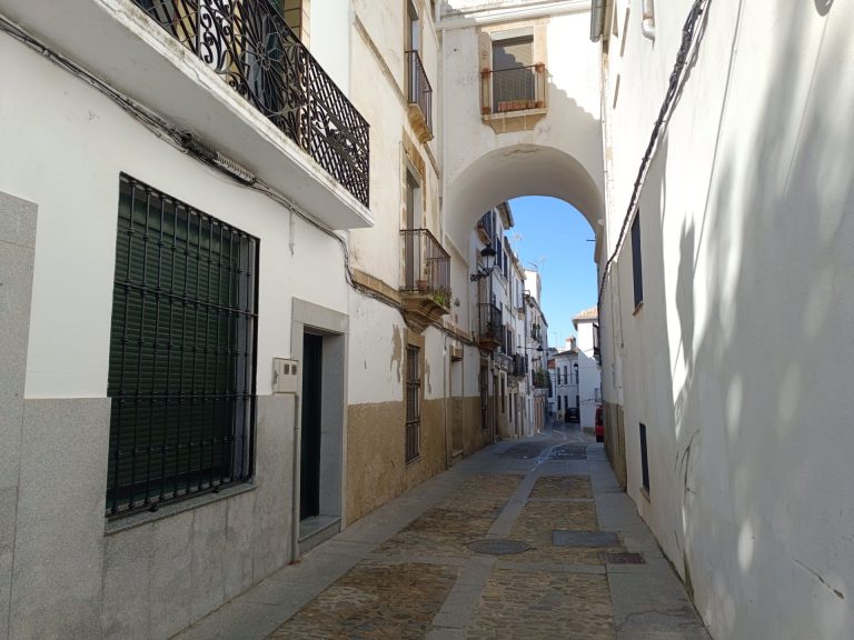 Explore the picturesque narrow alleyway with classic white arches in a charming European town.