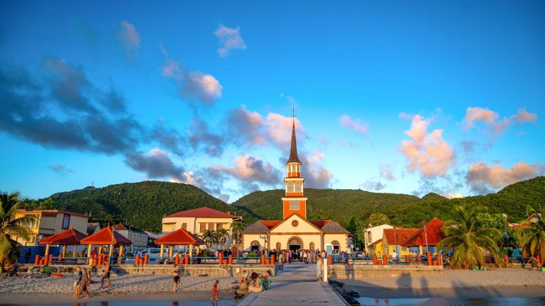 Vibrant tropical scene featuring a church, beach, and mountains during sunset.