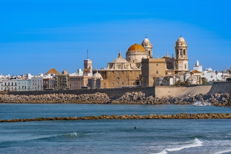 Scenic view of Cádiz Cathedral and waterfront, capturing iconic Andalusian architecture against a clear blue sky.