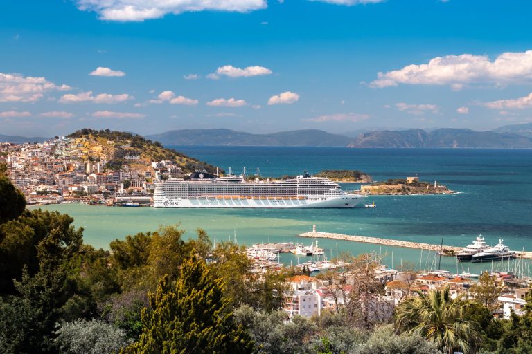 A cruise ship docked by the coastal town of Kusadasi, Turkey on a sunny day.