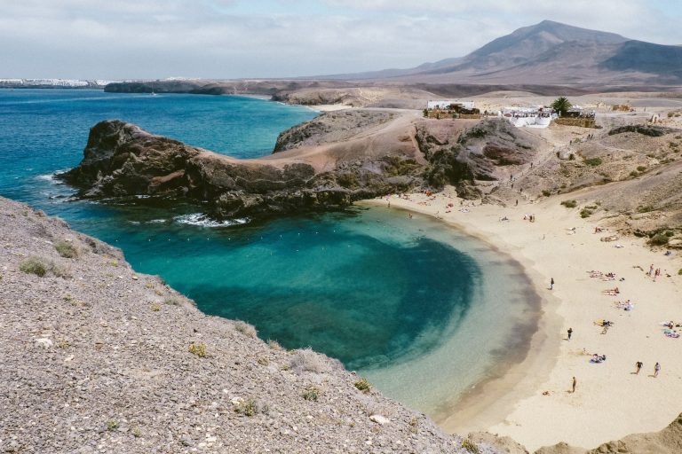 Breathtaking landscape of sandy shore near turquoise ocean water and rough rocky cliff