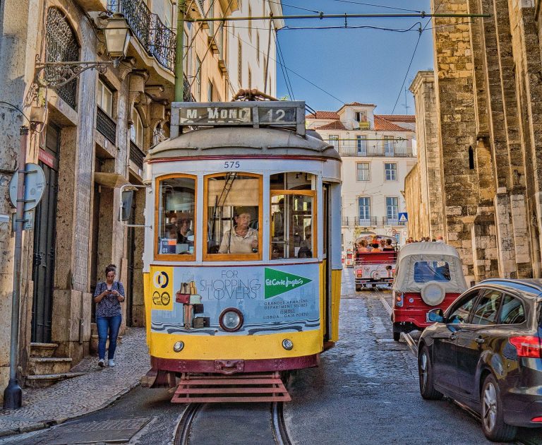 Vintage yellow tram navigating narrow streets of historic Lisbon, capturing city life.